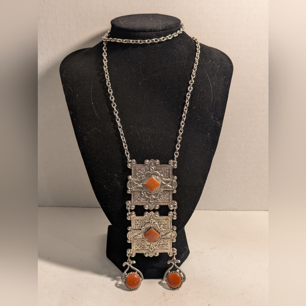 This is a silver-toned pendant necklace with red-orange cabochon stones.